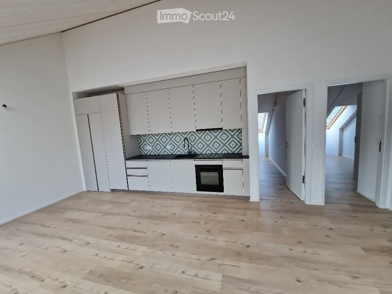 Empty kitchen with white cabinets, a black countertop, and a geometric tile backsplash. The floor is made of light wooden planks.