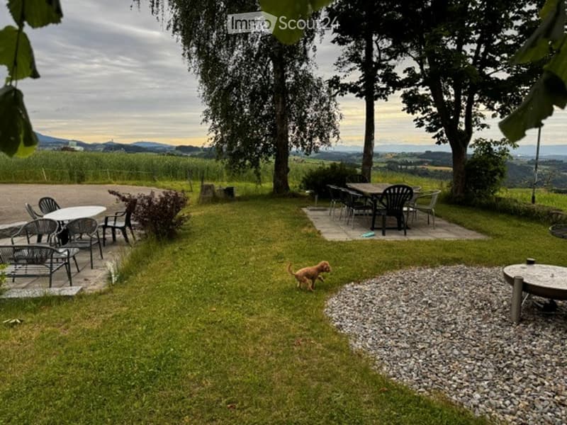 A spacious garden with a well-maintained lawn, scattered seating areas, and a scenic view of the countryside.