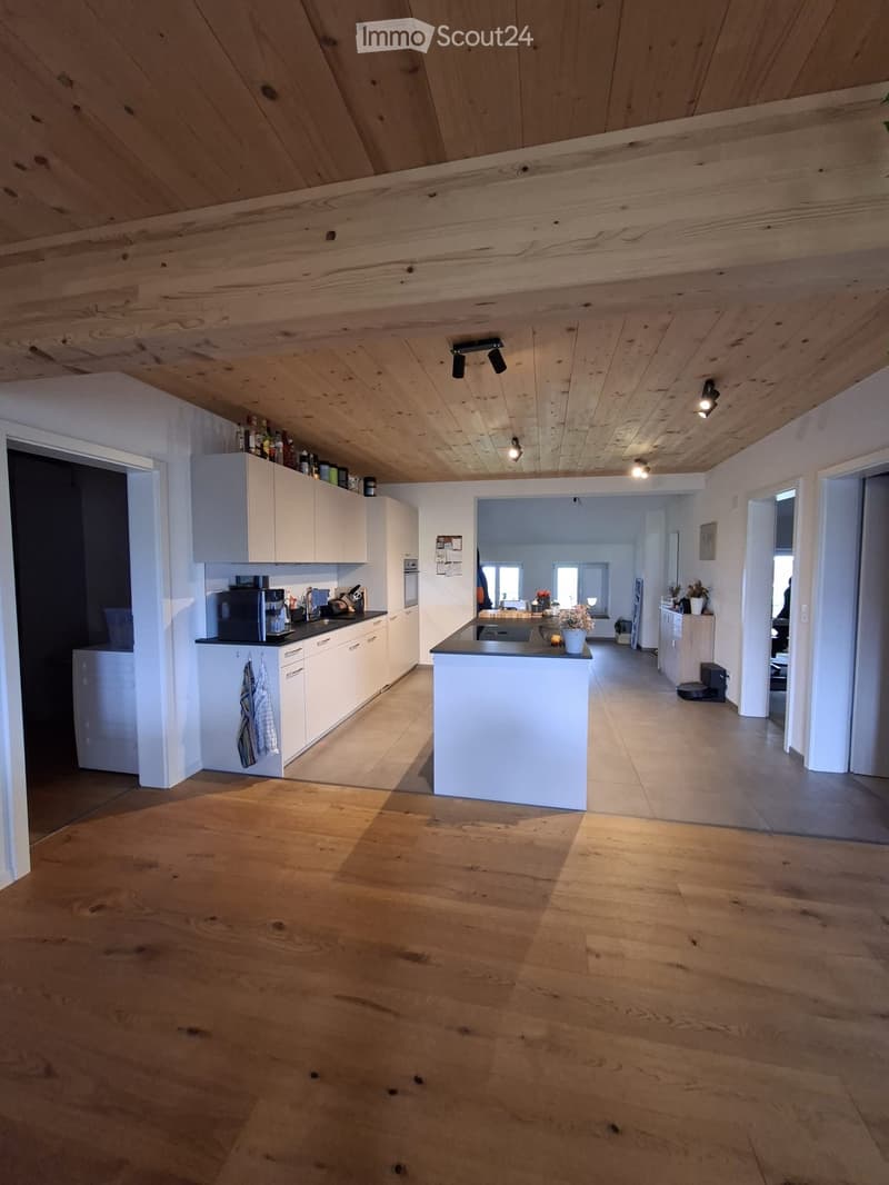 Modern kitchen with white cabinets, wooden floors, and a central island. Features include a coffee maker, microwave, and a vase with flowers on the island.