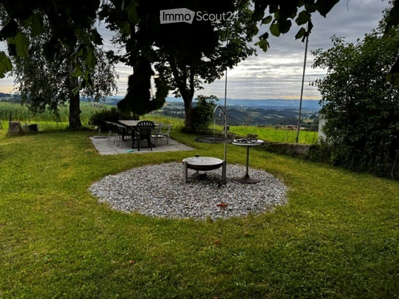 Lush green garden with a circular gravel area, outdoor dining set, and a scenic valley view.