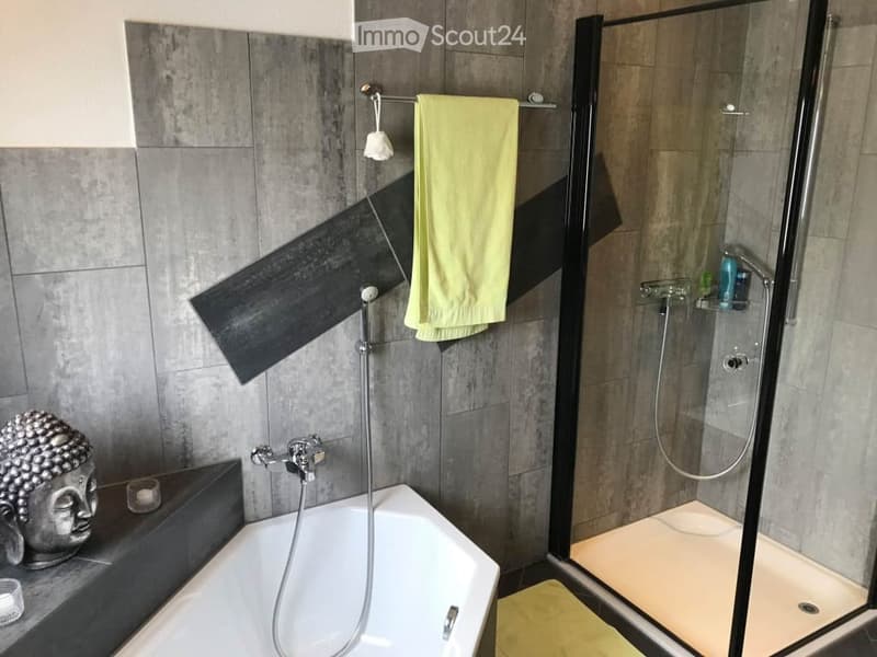Modern bathroom with a bathtub, glass-enclosed shower, towel rack, and decorative items including a statue and candles.