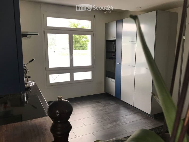 Modern kitchen with white cabinets, stainless steel appliances, large window, and dark tiled floor.