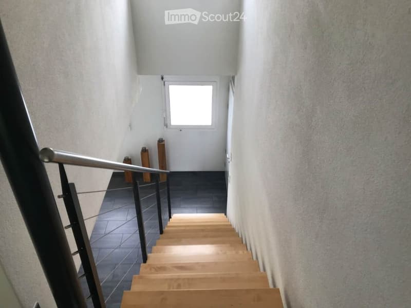 Modern hallway with wooden stairs, metal railing, and a small window at the top.