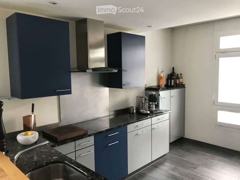 Modern kitchen with dark blue and white cabinets, stainless steel appliances, granite countertops, and various kitchen items including a coffee maker, cutting board, and bottles.