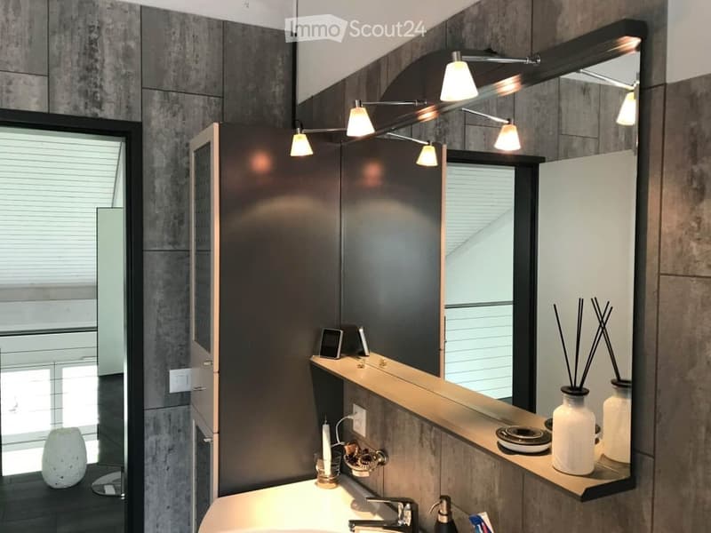 Modern bathroom with a large mirror, sleek lighting fixture, sink, and decorative vases on the counter.