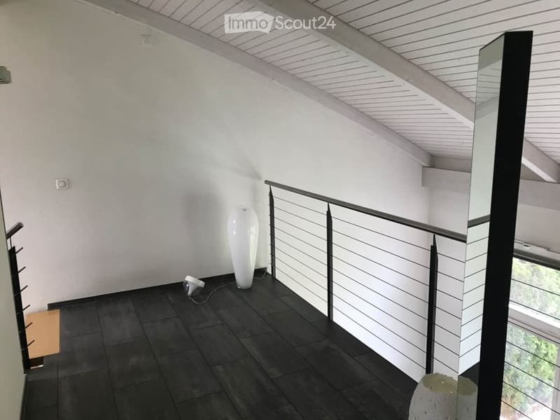 Modern hallway with dark tiled floor, white walls, and a sleek metal railing leading to an upper level. A tall white vase and a small lamp are placed on the floor.