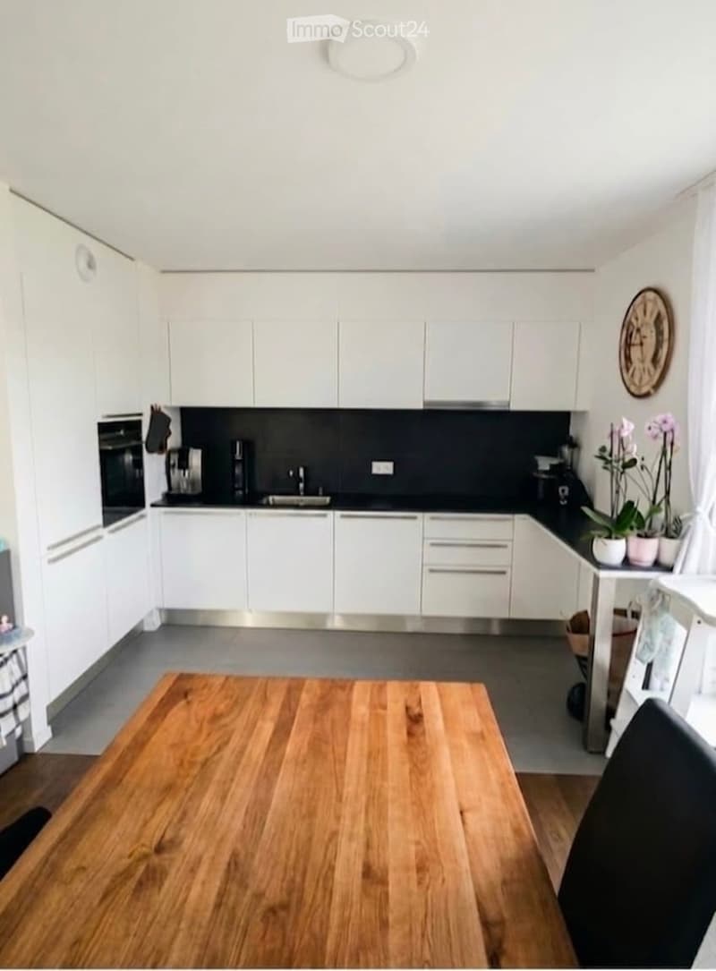 Modern kitchen with white cabinets, stainless steel appliances, and a wooden dining table with chairs.