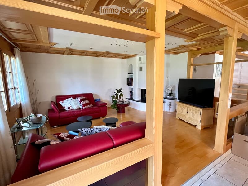 A modern living room with a red leather sofa, glass coffee table, small black stools, a flat-screen TV on a wooden stand, and a fireplace with a decorative plant on a side table.
