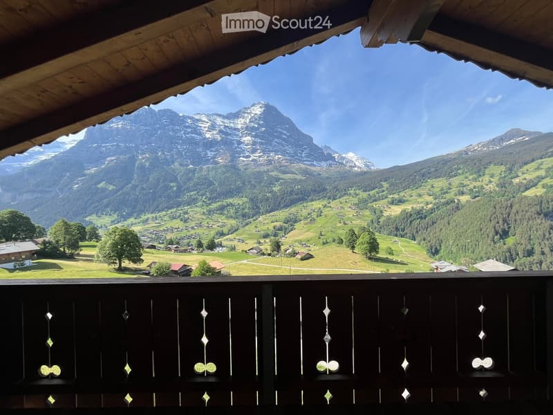 Balcony with wooden railing overlooking a scenic mountain valley and village below.