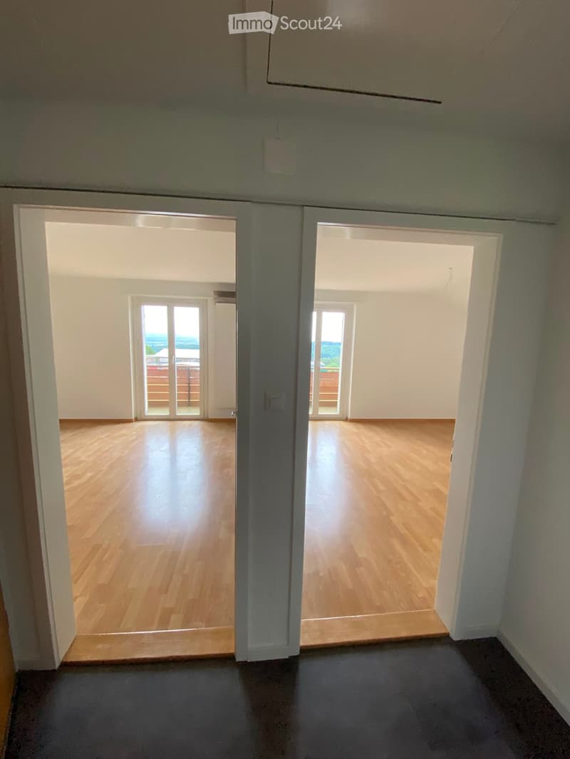 Empty hallway with wooden flooring, white walls, and open doors leading to rooms with large windows and balconies.