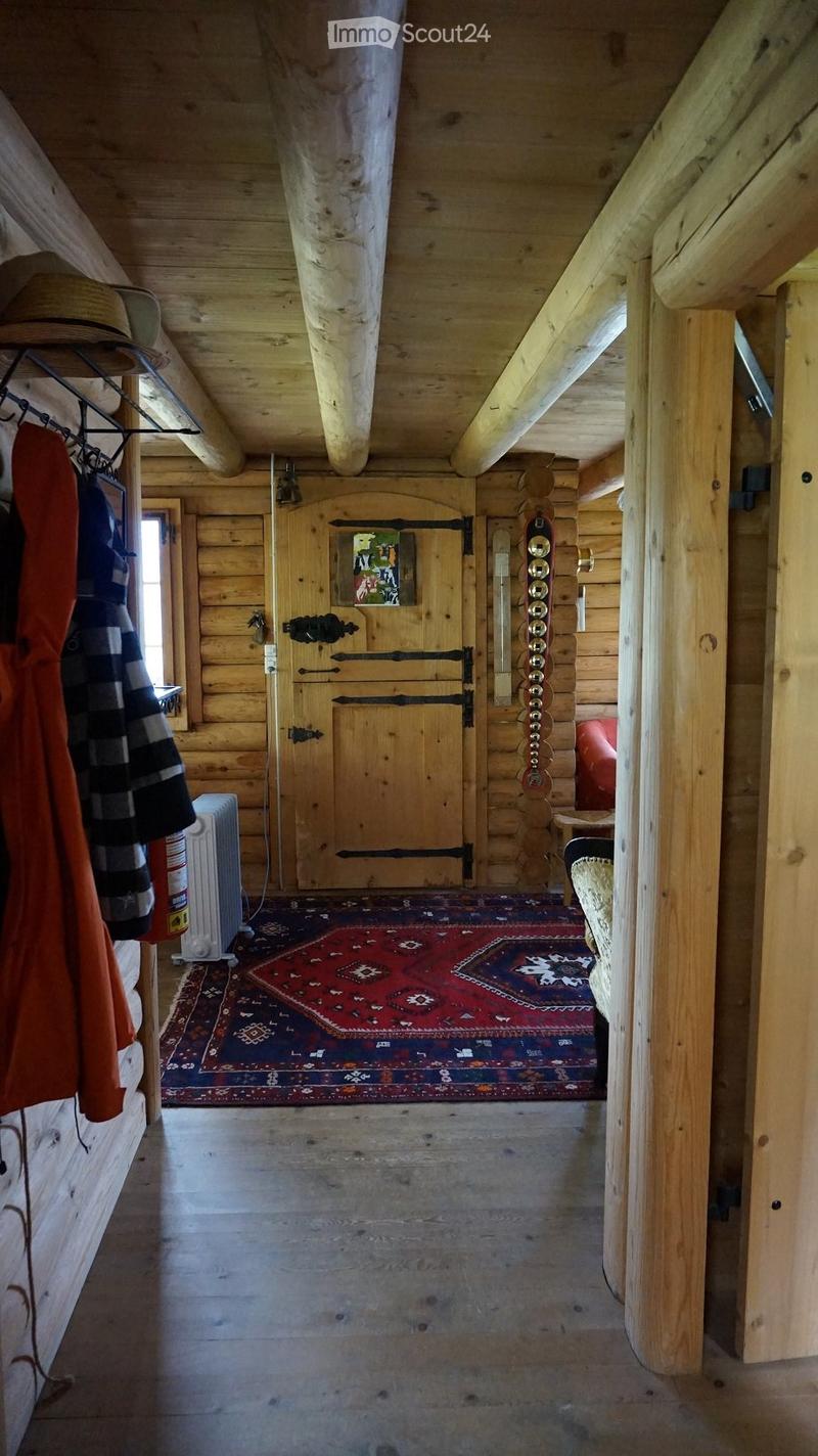A rustic wooden hallway with exposed beams, a radiator, a coat rack, a picture frame, and a small seating area with a chair and table.