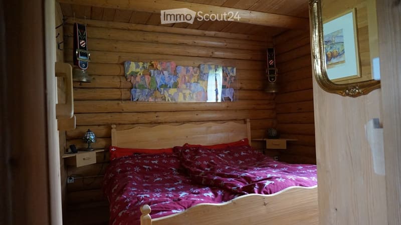 Cozy wooden bedroom with a wooden bed, red bedding, nightstand with lamp, mirror, and decorative items including skateboards and artwork.
