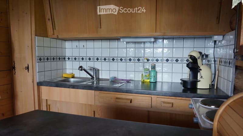A small kitchen with wooden cabinets, a black countertop, a sink with a faucet, and various appliances including a coffee maker and a stove.