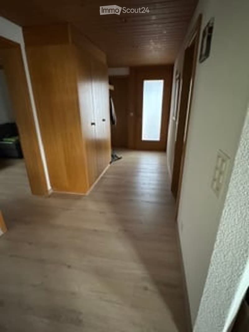 Empty hallway with wooden flooring, white walls, and a wooden wardrobe on the left side.