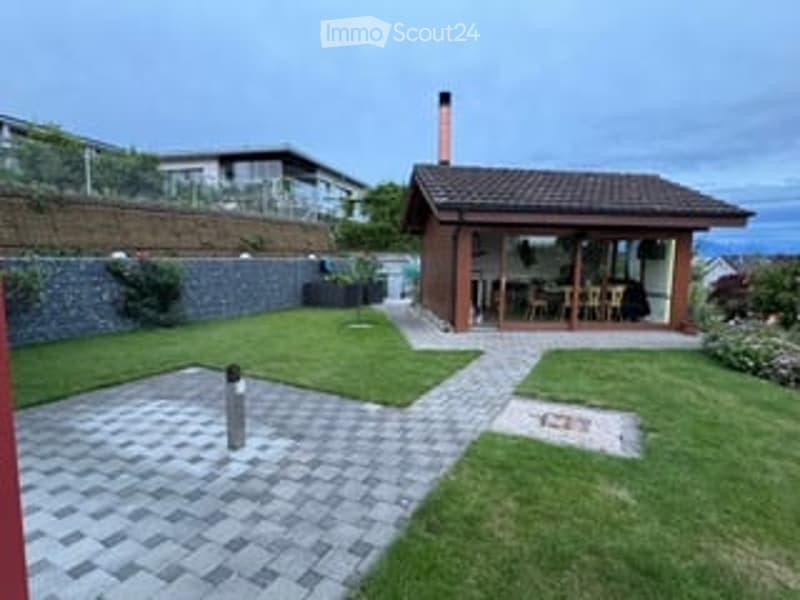 Well-maintained garden with a paved pathway, small wooden decked patio area, outdoor furniture, and scenic ocean view.