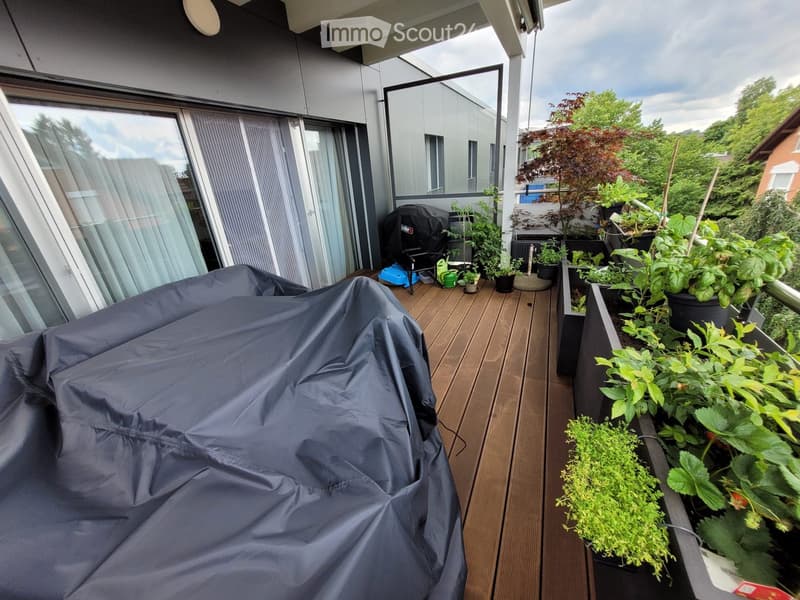 Wooden deck with covered furniture, potted plants, and a view of greenery.