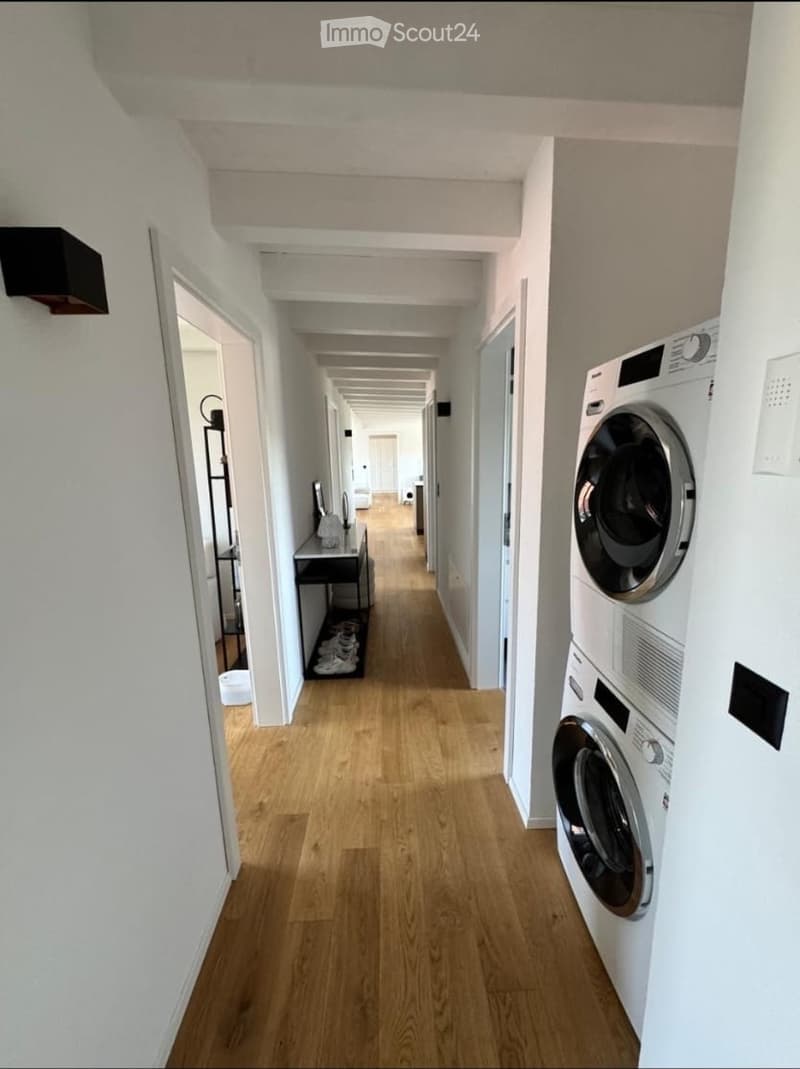 Long, narrow hallway with wooden flooring, white walls, and a private washing machine on the right side.