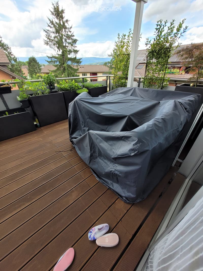 Wooden deck with covered furniture, potted plants, and a scenic view of trees and mountains.