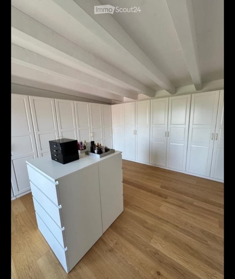 Bright, airy room with white cabinets and a grey countertop, featuring a wooden floor and slanted ceiling.