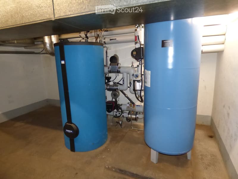 Utility room with two large blue water tanks, pipes, valves, and control units.