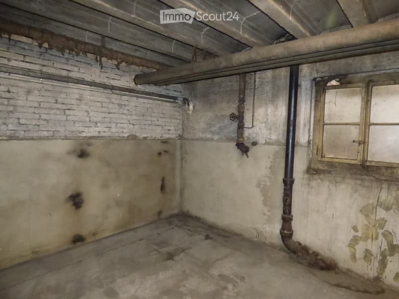 Empty basement room with exposed brick walls, concrete floor, pipes, and a small window.