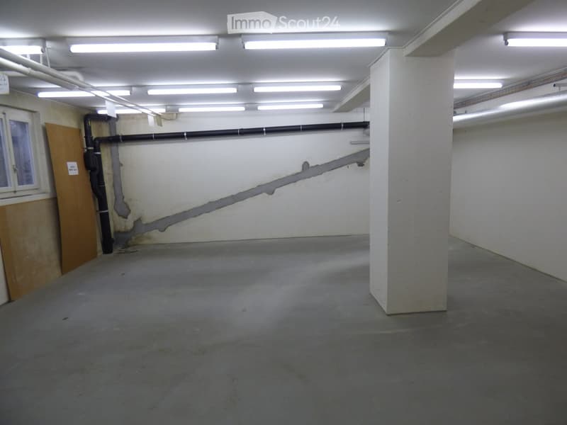 Empty underground parking space with concrete floor, white walls, support pillar, and fluorescent lighting.