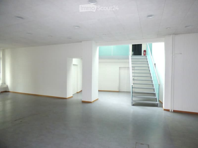 Empty room with white walls, grey concrete floor, and a staircase leading to an upper level.