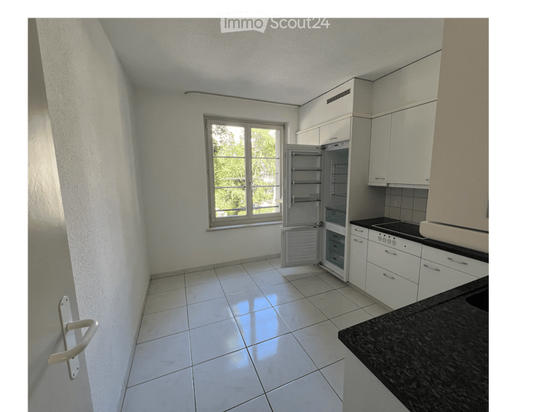 Modern kitchen with white cabinets, a black countertop, and an open refrigerator. The room features tiled flooring and a window offering a view of greenery outside.