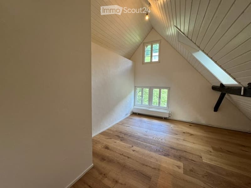Empty attic room with wooden flooring, white walls, and skylight windows. No furniture or equipment present.