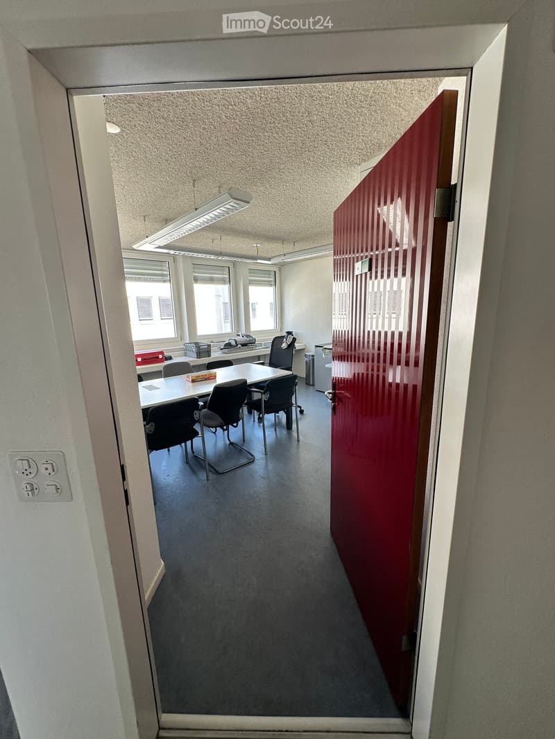 Office space with a table, chairs, printer, and cabinet, viewed through an open doorway.