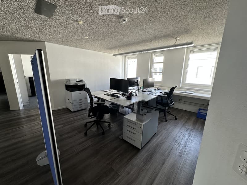 Office space with wooden flooring, two desks, two chairs, two computer monitors, a printer, and a small cabinet.