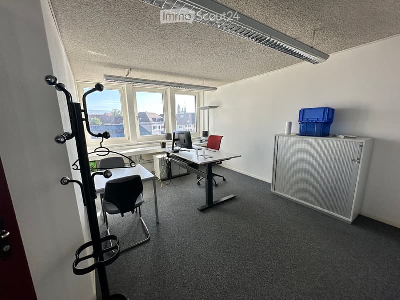 Office space with desks, chairs, computer, cabinet, and storage boxes. Large windows provide natural light and a view of the city.