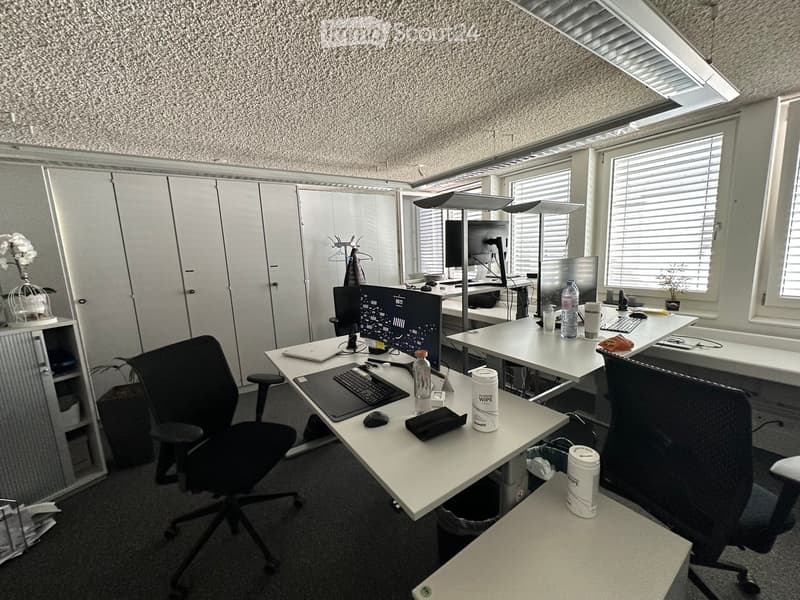 Office space with desks, chairs, multiple computer screens, keyboards, and various office supplies.
