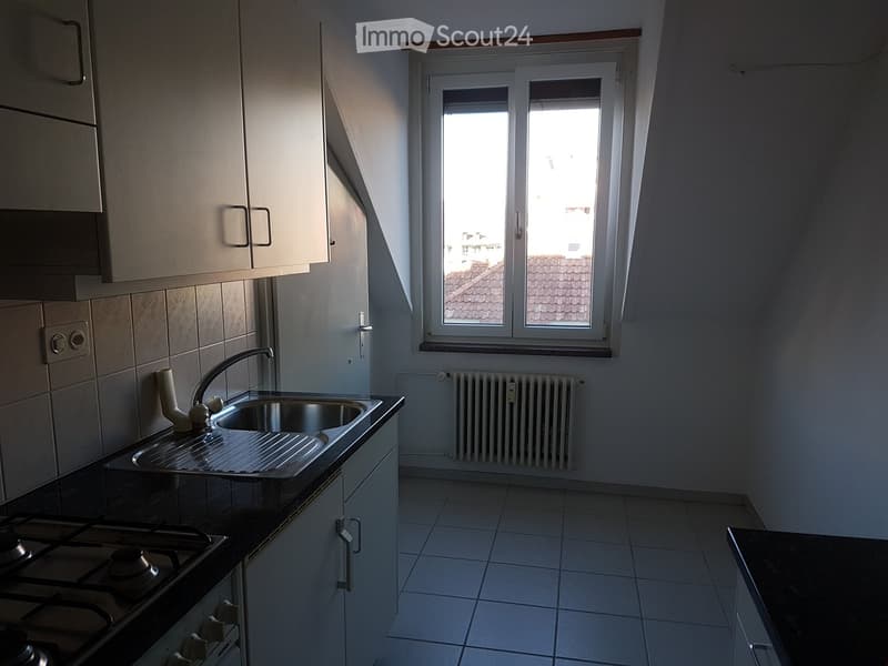 Modern kitchen with white tiled walls, stainless steel sink, gas stove, and built-in cabinets. Natural light from a window overlooking a roof.
