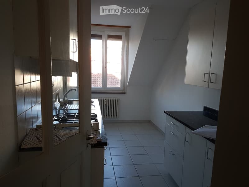 Compact kitchen with white tiled floor, white cabinets, black countertop, sink, faucet, stove, and radiator.