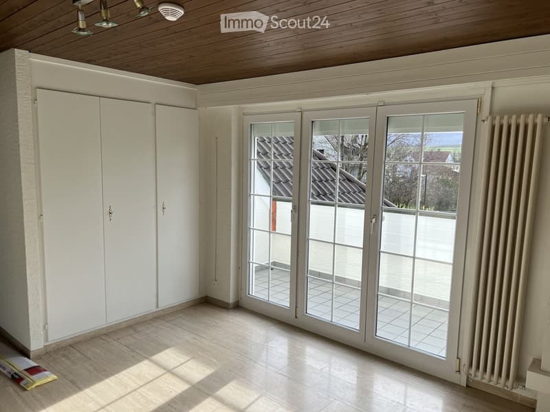 Empty room with white walls, tiled floor, large sliding glass doors leading to a patio, built-in white cabinets, and a radiator on the right side.