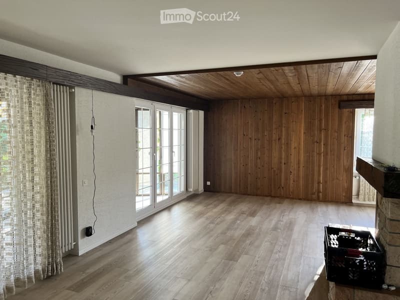 Empty room with wooden flooring, wooden panel walls, large glass doors, and a wooden ceiling. No furniture or equipment present.