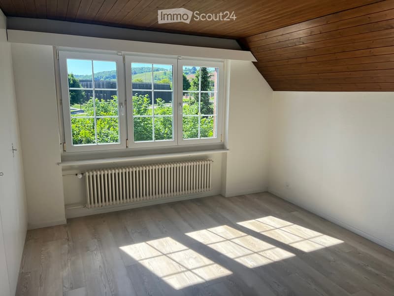 Empty room with wooden flooring, white walls, large windows, and a radiator beneath the windows.
