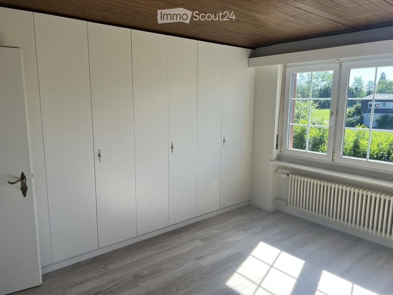 Empty room with white built-in wardrobes, wooden flooring, and large windows letting in natural light.