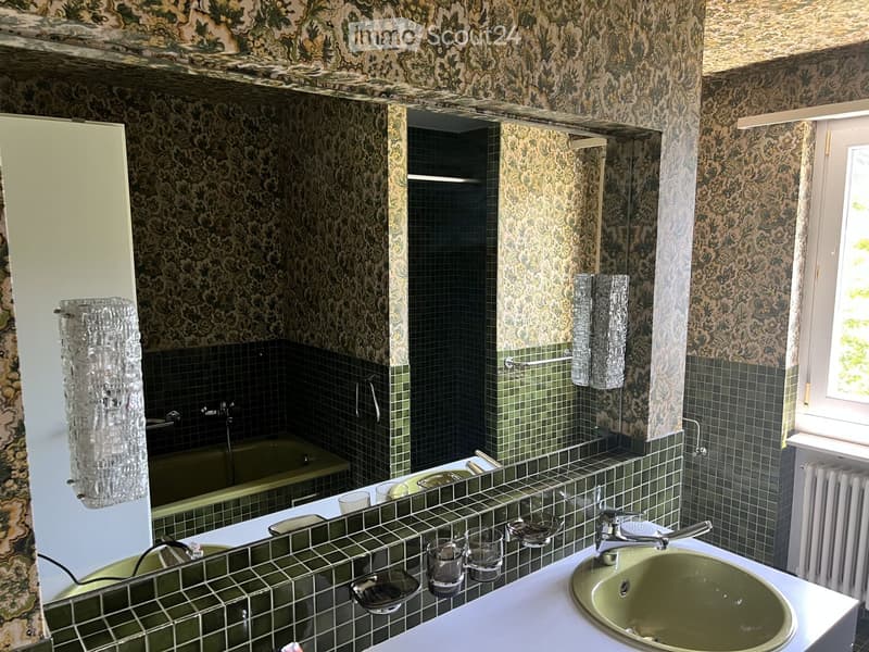 Bathroom with green tiles, floral wallpaper, sink, mirror, bathtub, and towel.