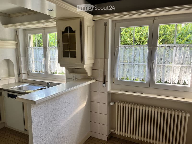 Modern kitchen with white cabinets, granite countertop, sink, and radiator under windows with lace curtains.