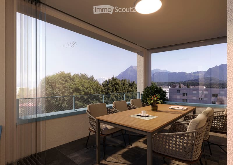 Balcony with a wooden table, chairs, a potted plant, and a cup, overlooking a scenic mountain view.
