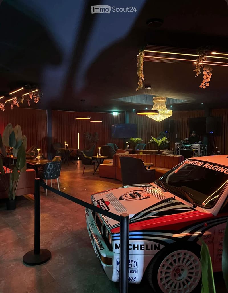 A stylish lounge area with a vintage racing car prominently displayed, featuring comfortable seating, a television, and decorative lighting.