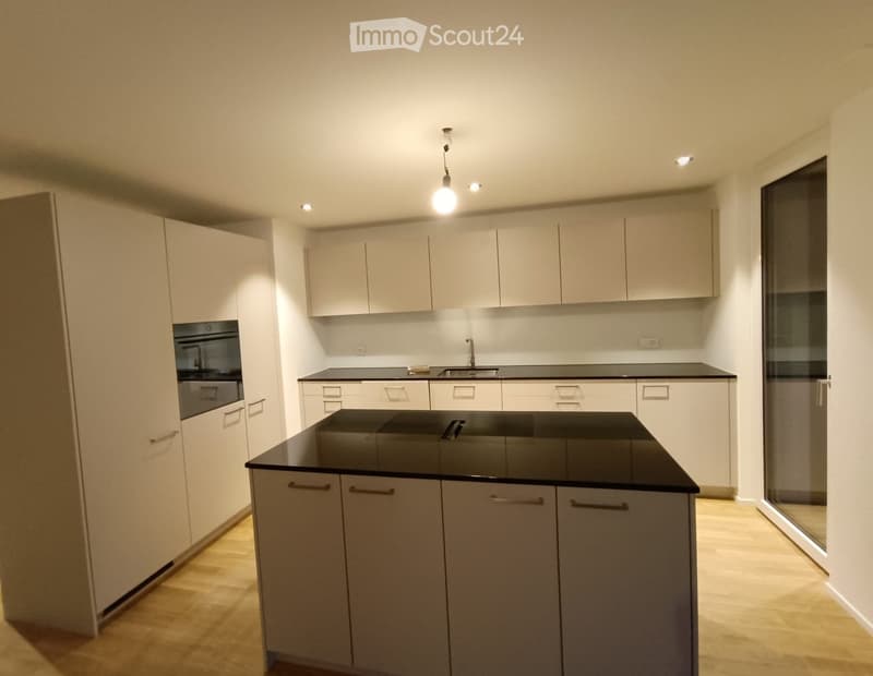 Modern kitchen with white cabinets, black countertops, and a central island. Features a sink, faucet, and pendant light fixture.
