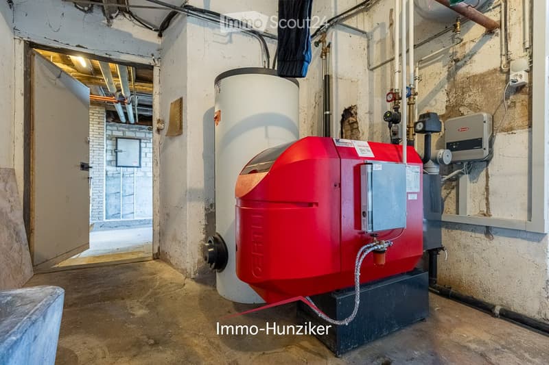 Utility room with a red boiler, water heater, and various pipes and valves.