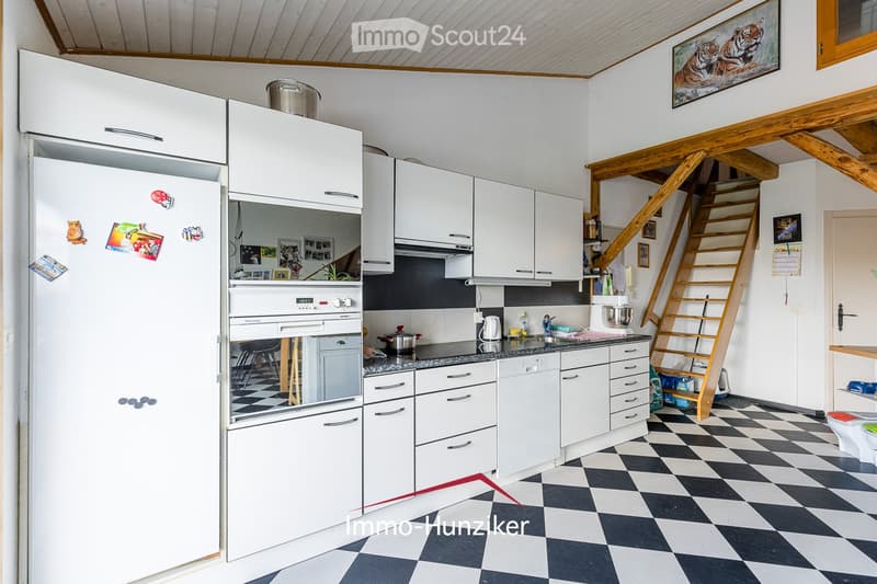 Modern kitchen with white cabinets, stainless steel appliances, black and white checkered floor, and a wooden staircase leading to an upper level.