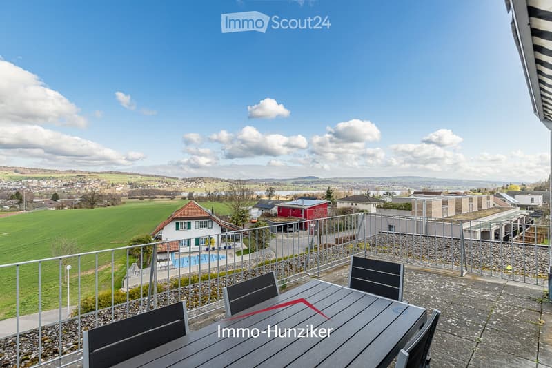 Balcony with a view of a town and countryside, featuring a table and chairs.