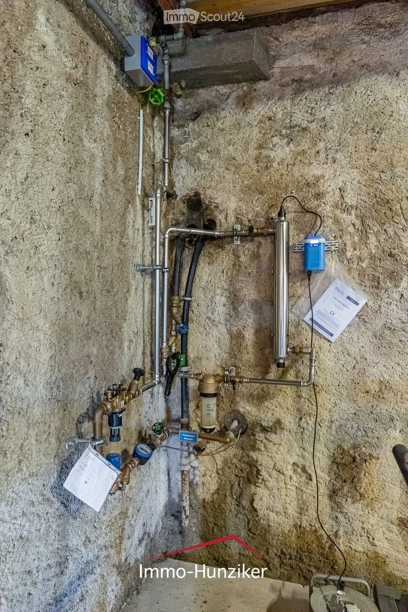 A utility area with exposed concrete walls, various pipes, valves, filters, and control units installed for water management.