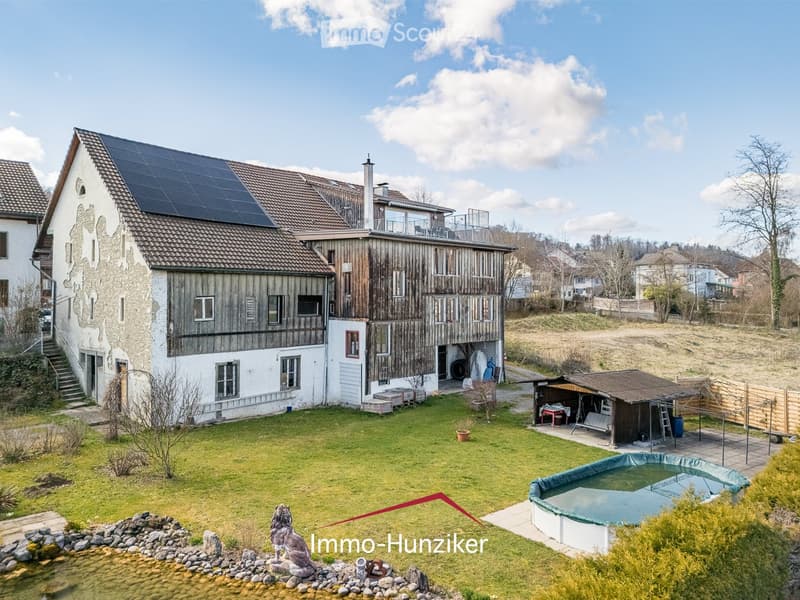 Two-story house with solar panels on the roof, surrounded by a well-maintained garden, a swimming pool, and a small shed.