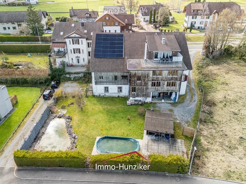 Aerial view of a residential house with a tiled roof, solar panels, a swimming pool, and surrounding greenery.